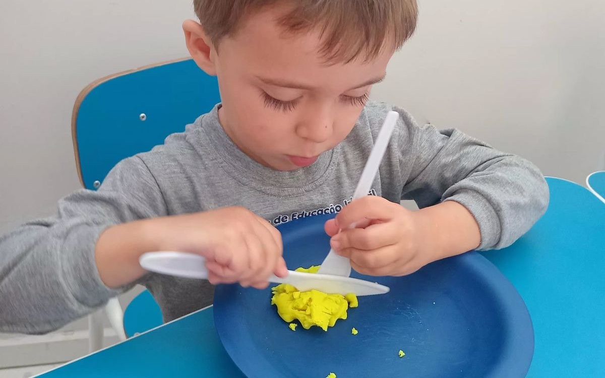 Criança treinando o uso de garfo e faca